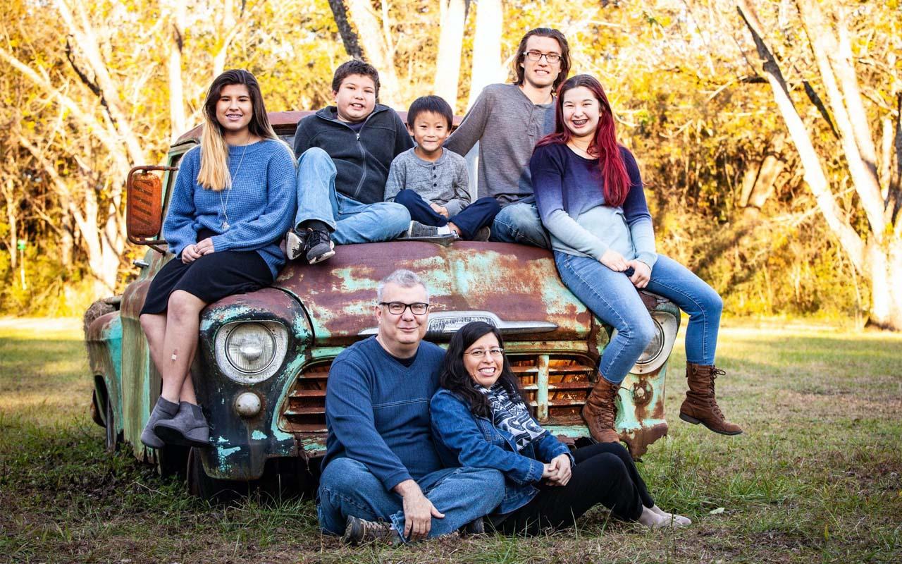 Keith and Rachel Murphy and their children posing with a rusted down car near the woods.