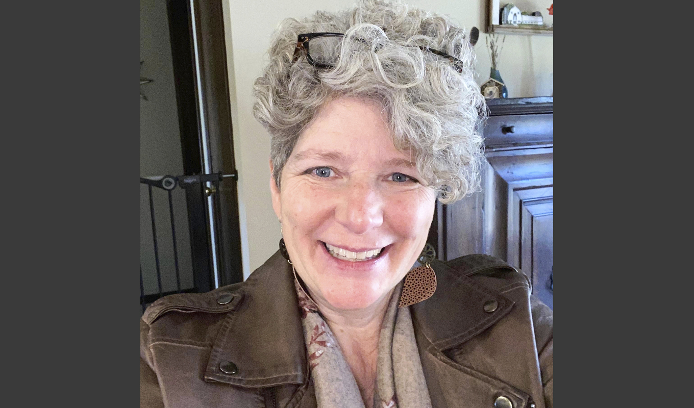 A woman with gray hair and glasses smiles at the camera.