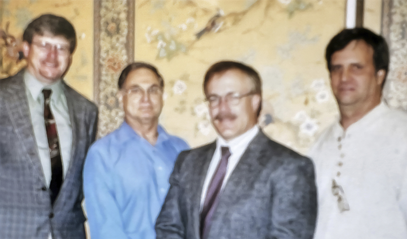 Four individuals posing in front of a decorative wall, appearing in professional attire.