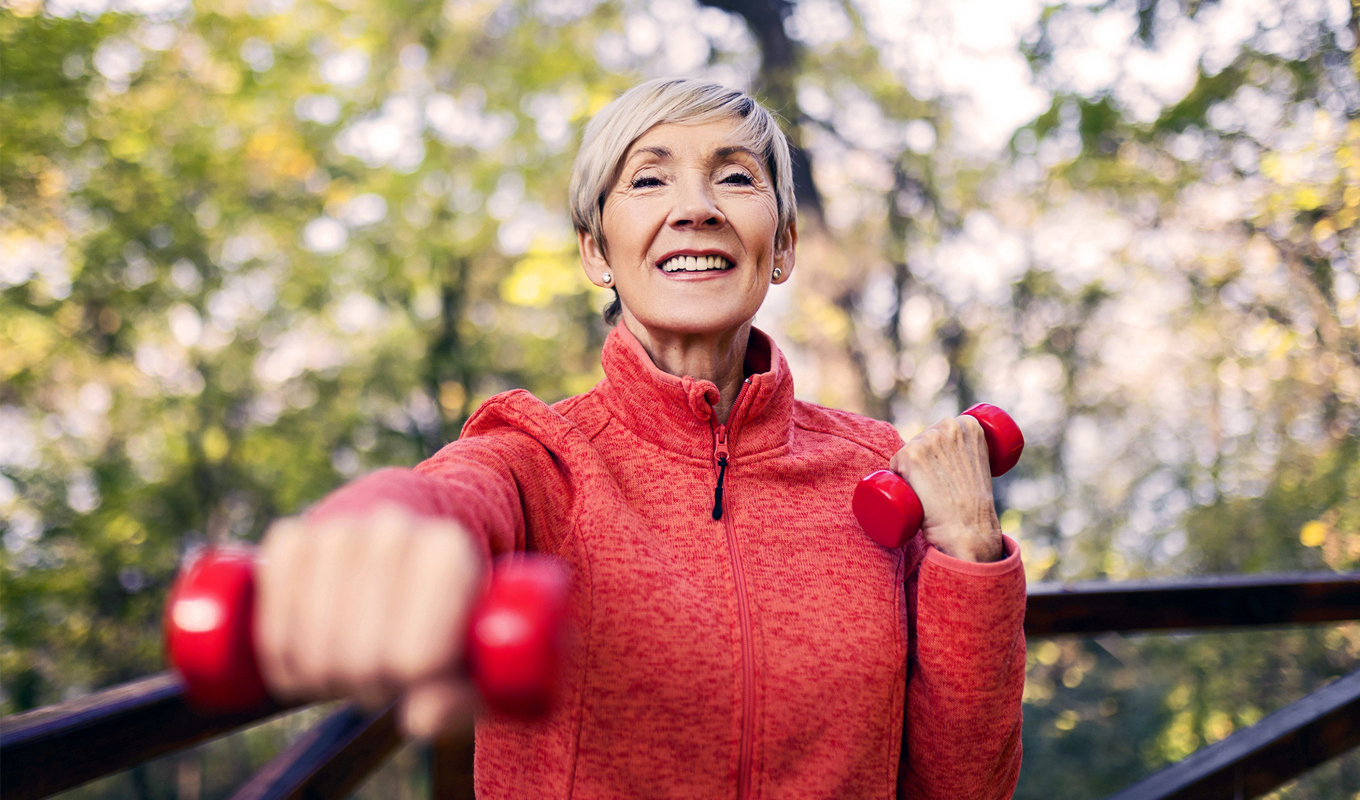 Smiling woman in red sweater holds a small handweight.