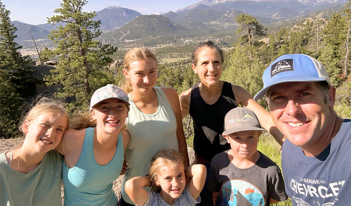 A family of seven poses in front of a scenic backdrop in the mountains.