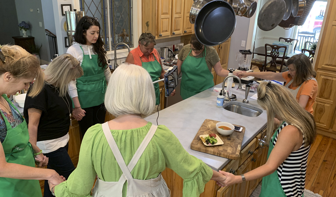 Several family members praying and holding hands around a kitchen