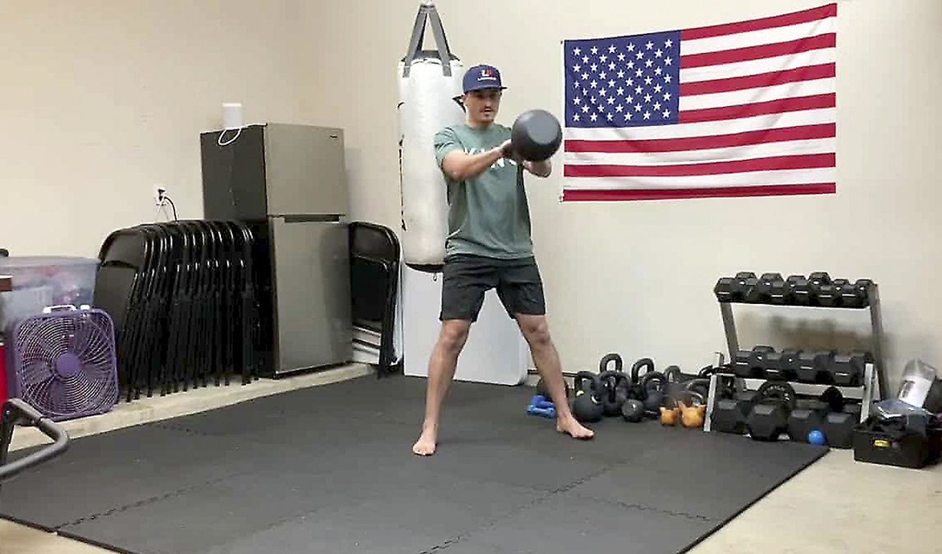 A man in a home gym swings a kettlebell forward.