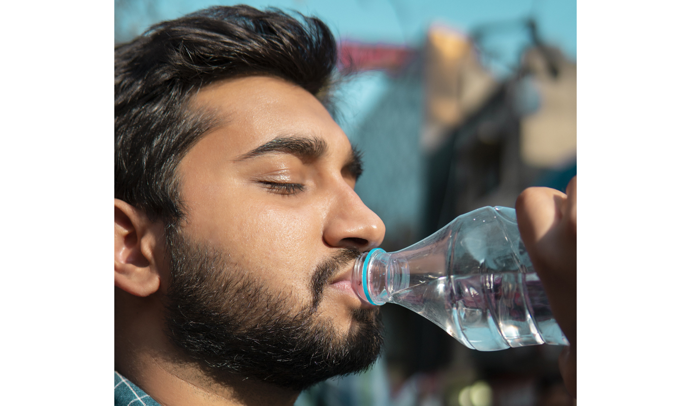 Man drinking water from a bottle outdoors with sunlight illuminating his face.