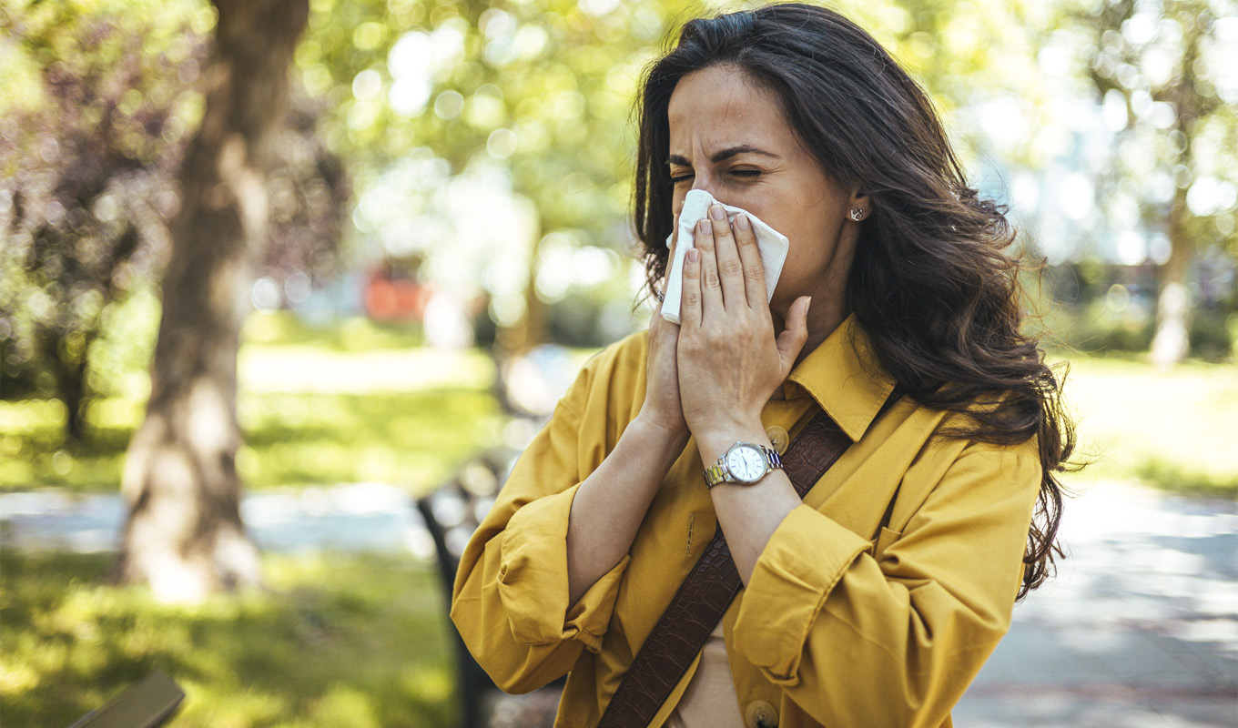 Woman in an outdoors setting wipes her nose after sneezing.