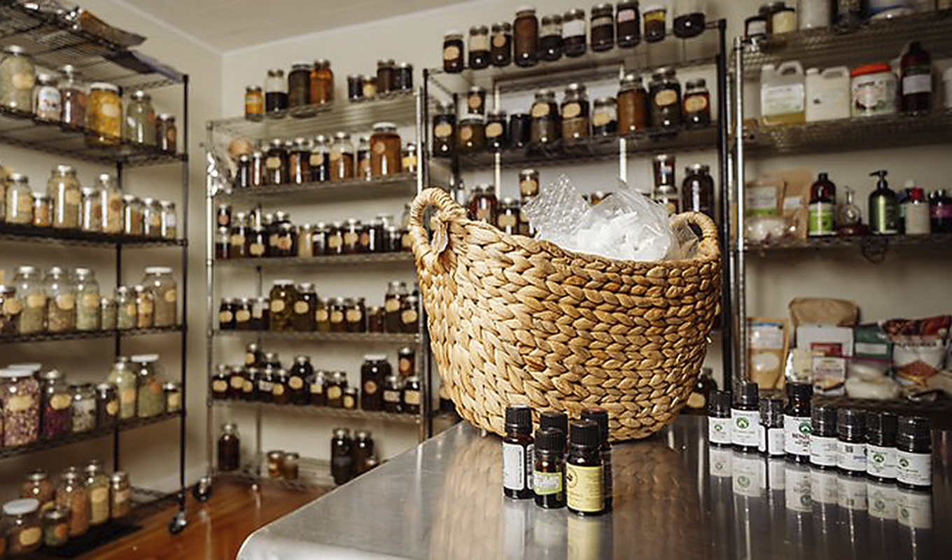 Interior of a modern apothecary shop featuring shelves stocked with labeled jars and bottles, a wicker basket with products placed on a metal table in the foreground.
