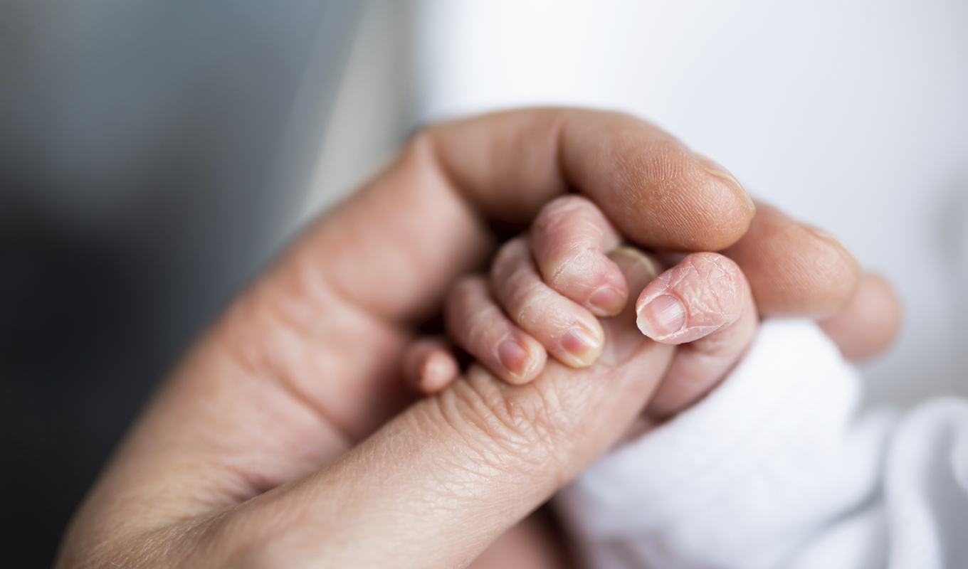 A close-up of a person’s hand cradling a tiny baby’s hand, illustrating tenderness and affection.