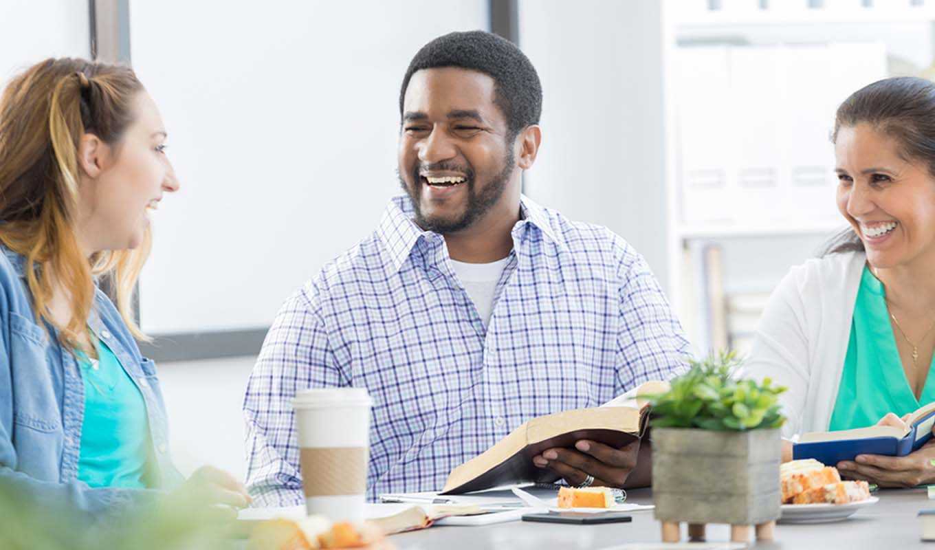 Three people laughing and studying the Bible while enjoying a snack