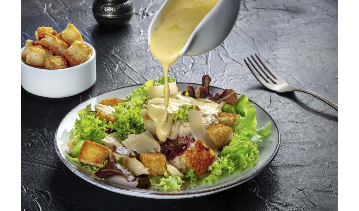 A fresh salad topped with cheese, as creamy dressing is poured over it, enhancing its vibrant colors and textures.