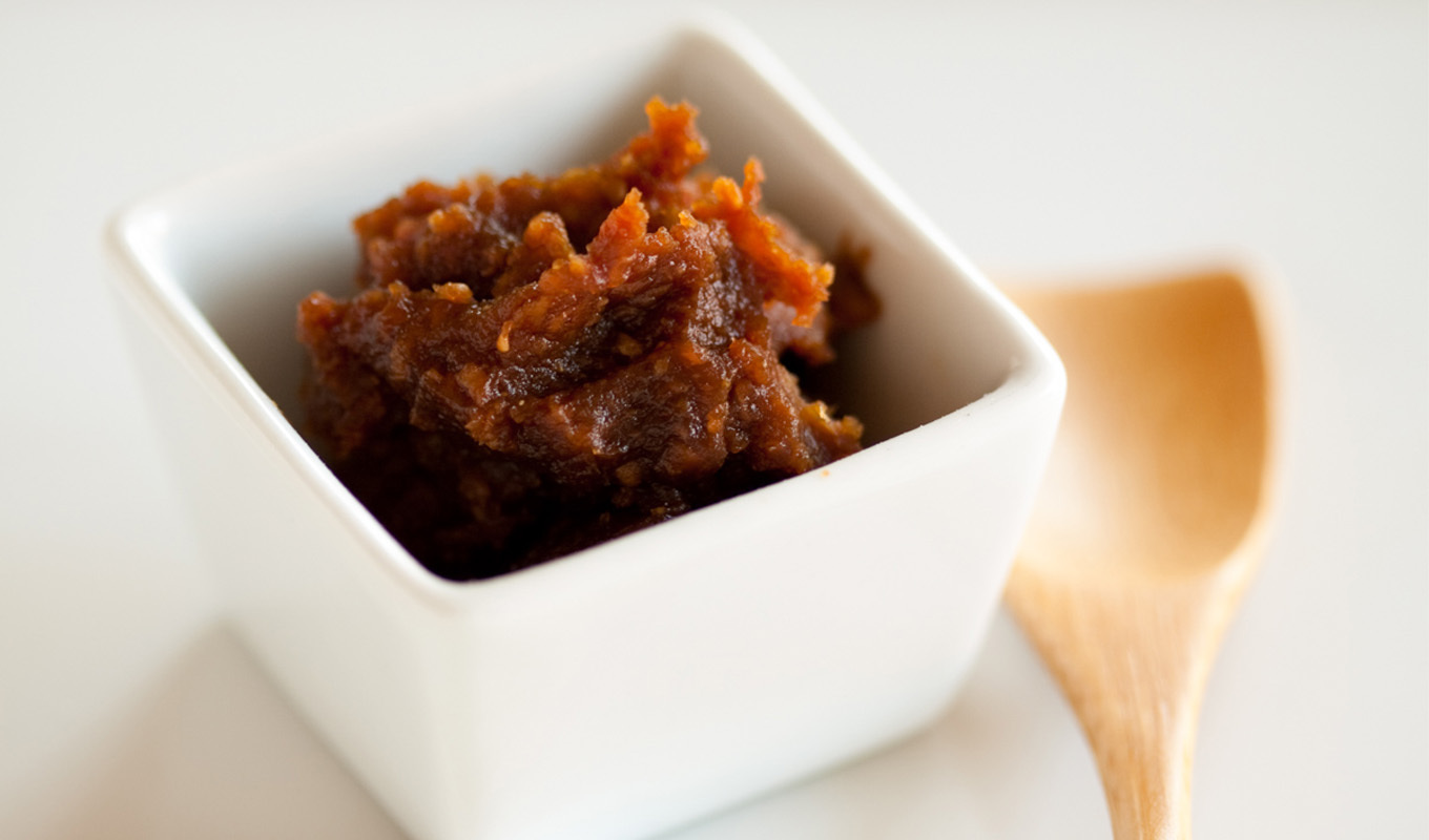 Thick date paste in a small white dish beside a wooden spoon.