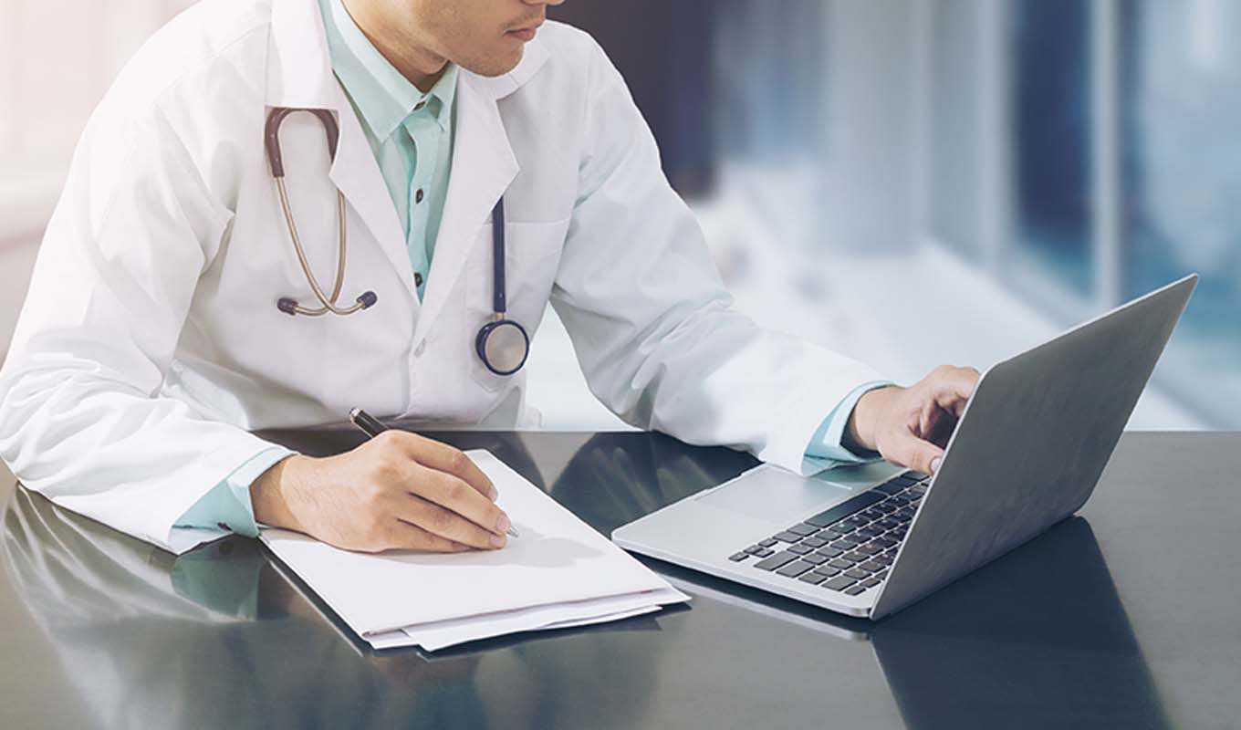 Doctor taking notes and reviewing information on a laptop