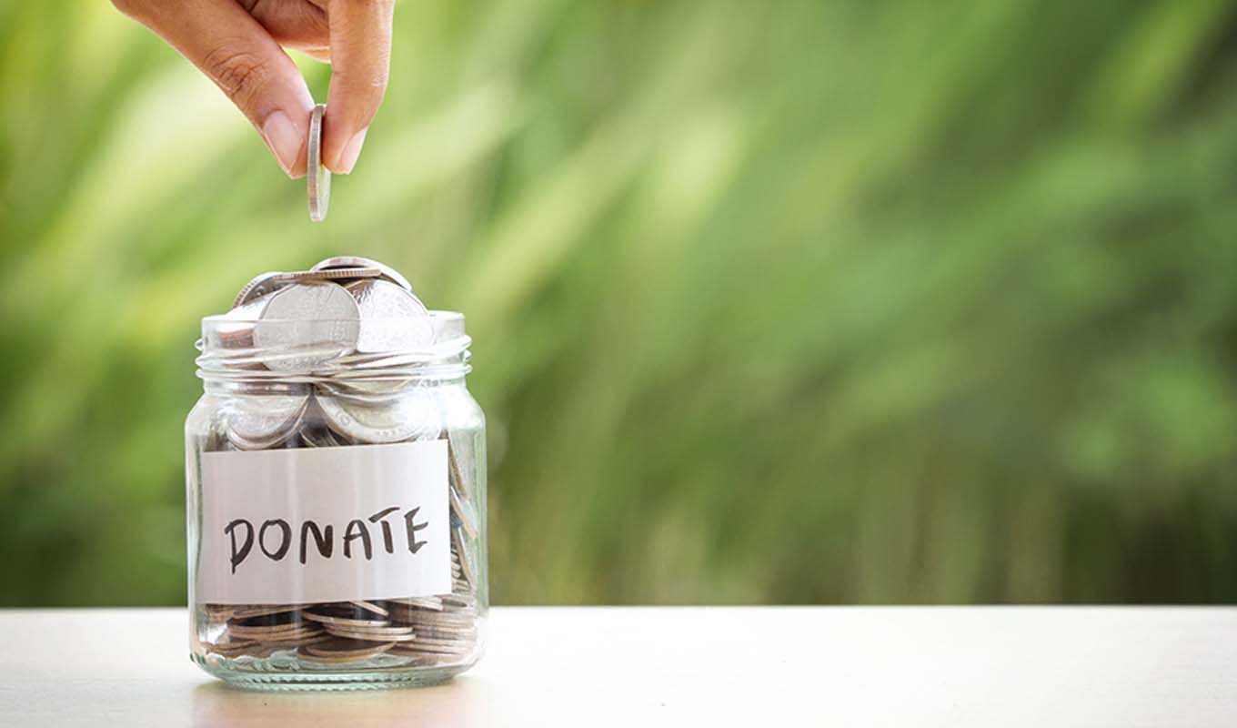 A person placing a coin into a donation jar