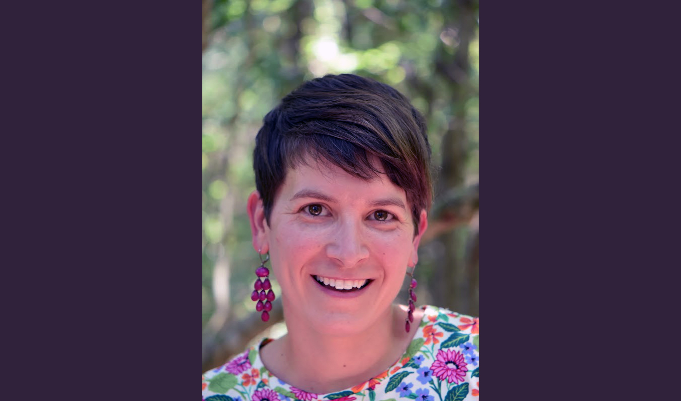 A person with short, dark hair is wearing a colorful floral-patterned top featuring pink, purple, and green flowers.