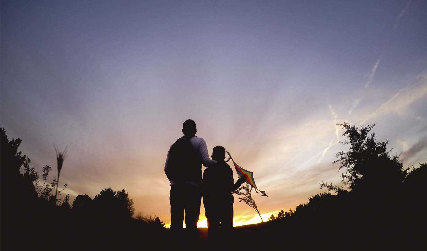 Father and young son flying a kite at sunset