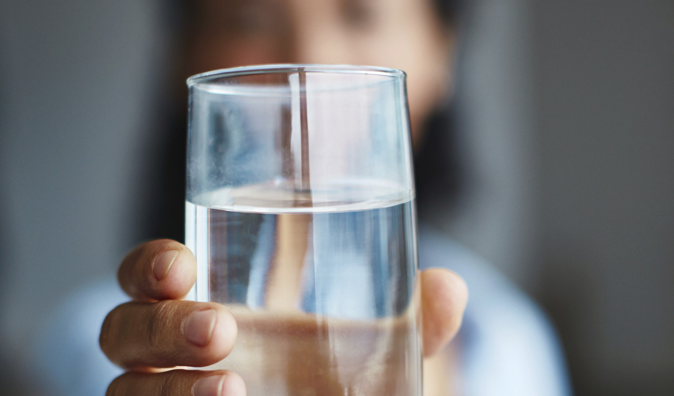 A person smiling while holding a clear glass of water, ready to take a refreshing sip.