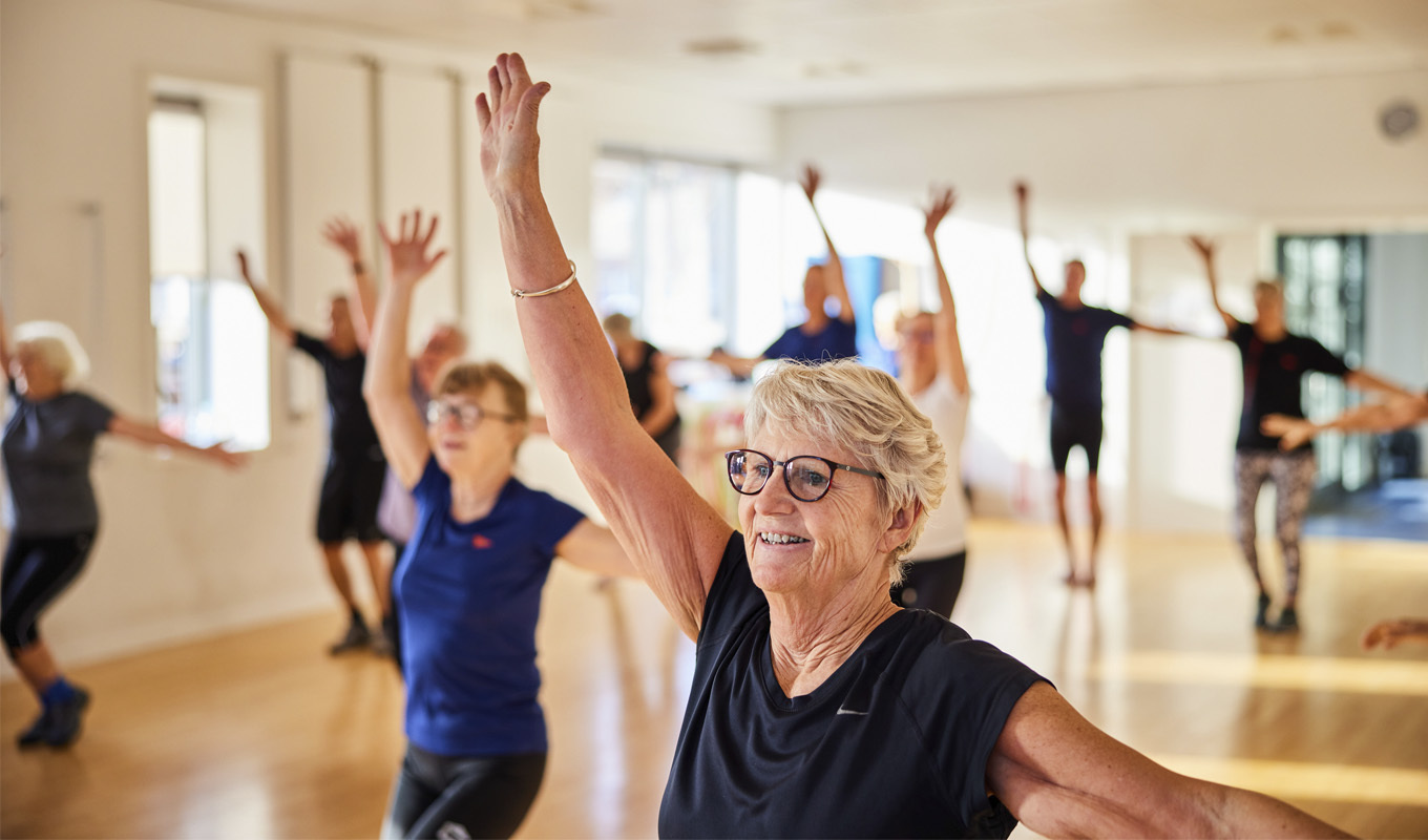 Women and men raise their arms as they exercise in a class.