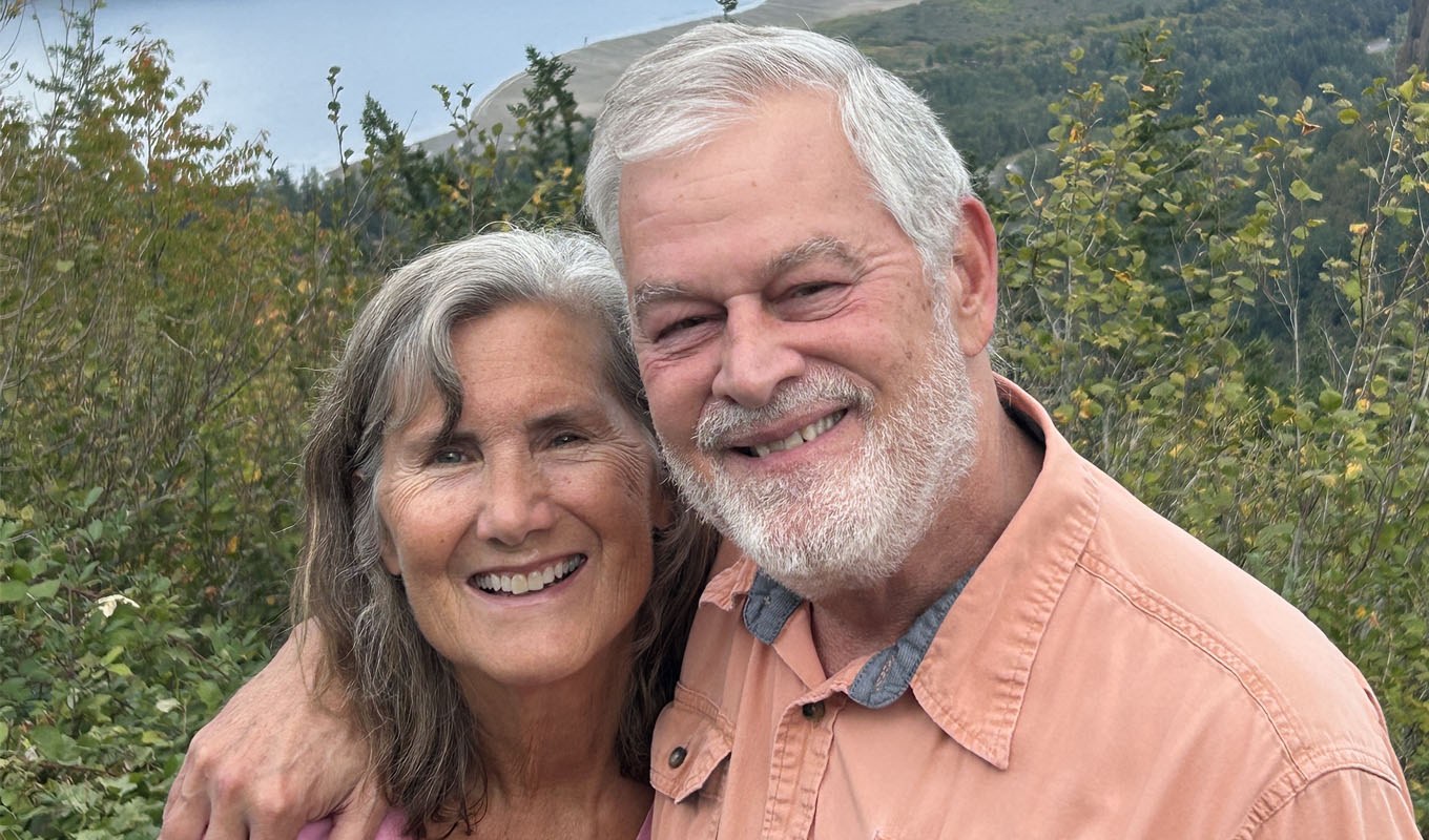 A woman and man stand in front of a hillside of wildflowers.