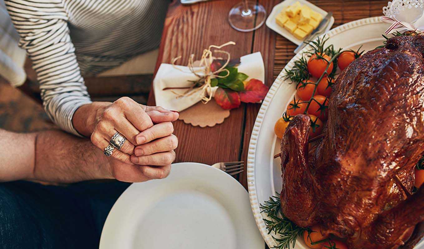 A couple praying before a turkey dinner