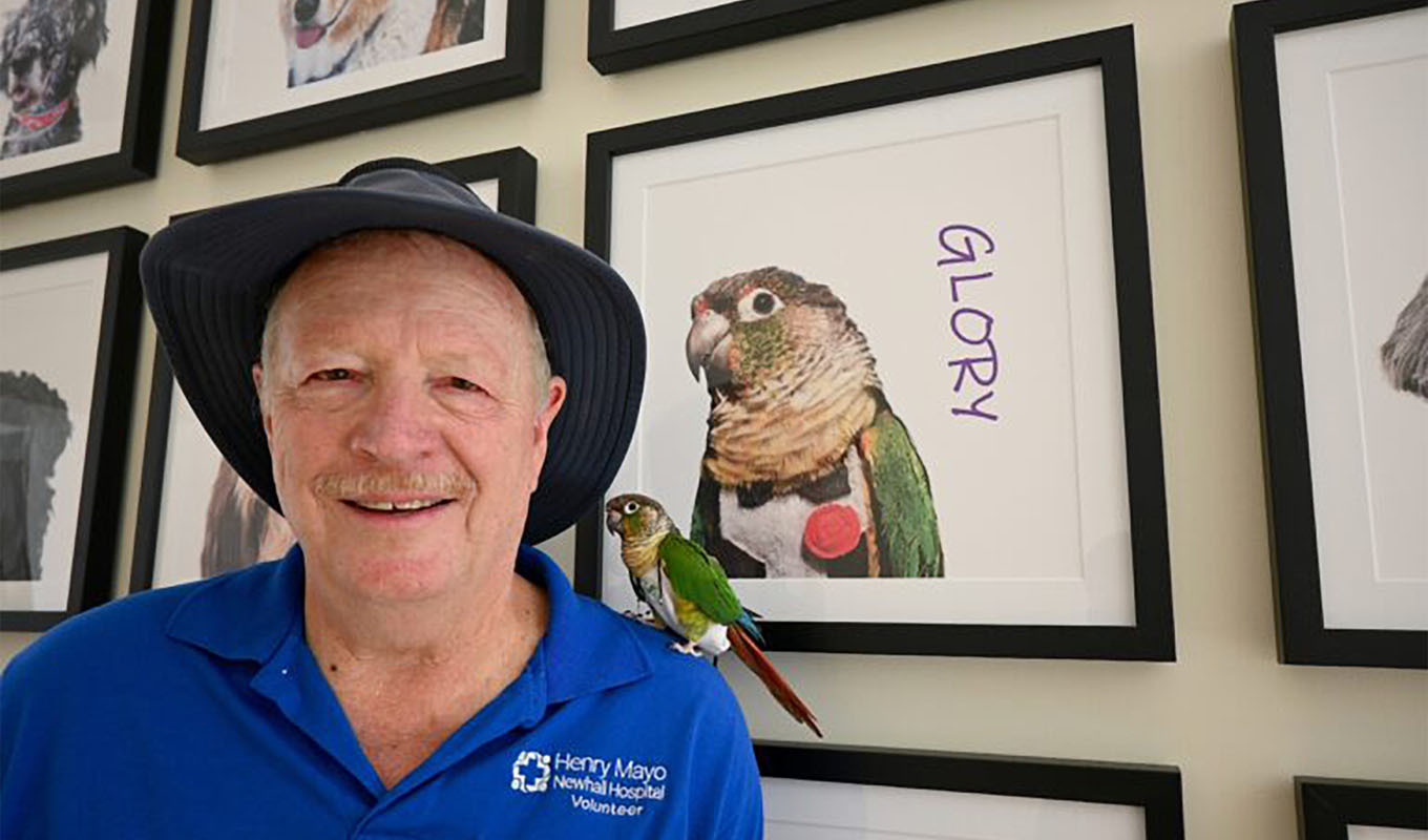 Volunteer with therapy parrot perched on shoulder at hospital, showcasing animal therapy ministry and sharing Christian encouragement with patients