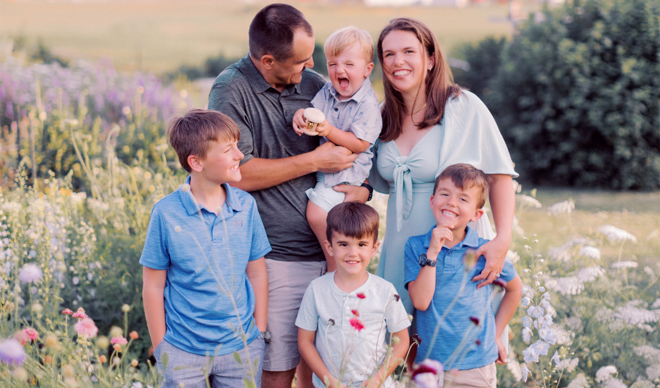 Family standing together in a wildflower field, with parents and children gathered closely outdoors.