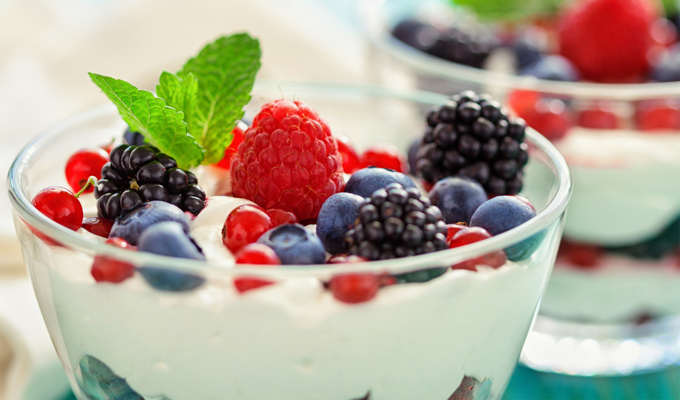 Glass bowl of Greek yogurt topped with fresh raspberries, blackberries, blueberries, red currants, and a mint leaf.
