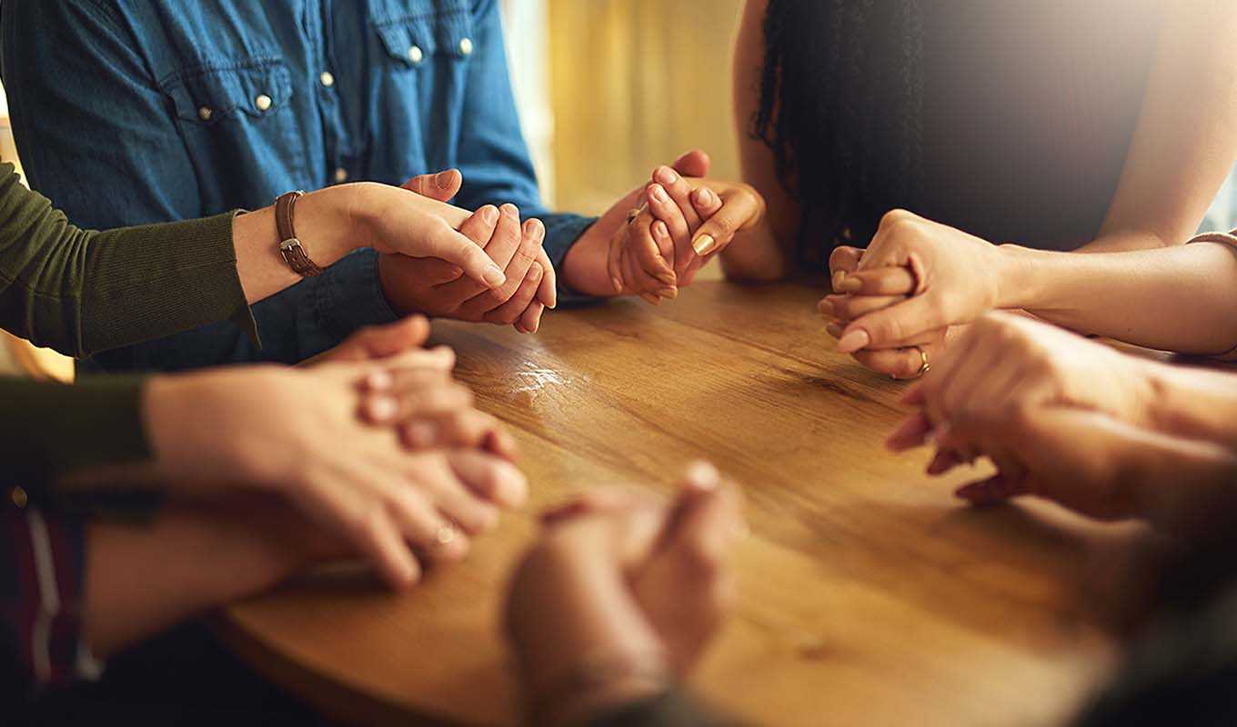 A group holding hands around a table, praying