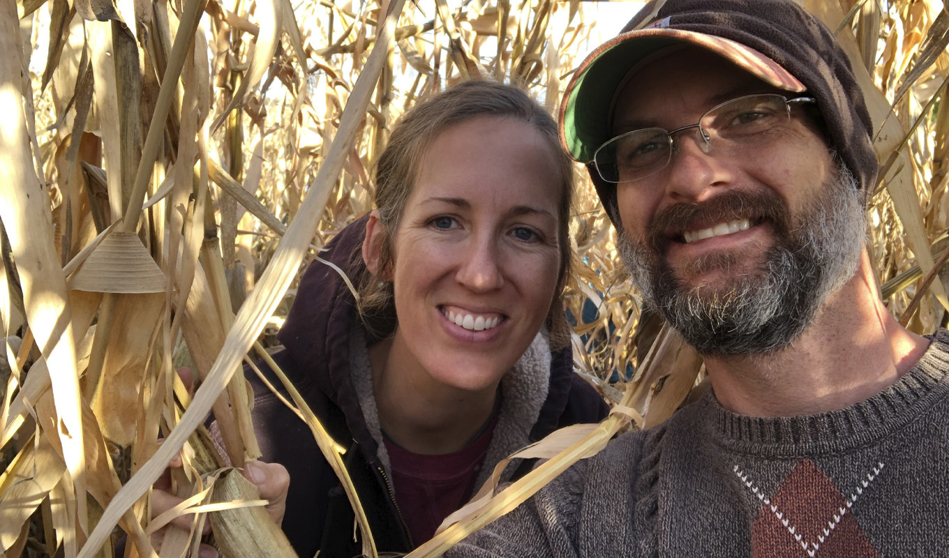 Smiling woman and man in cornfield taking selfie during daytime.