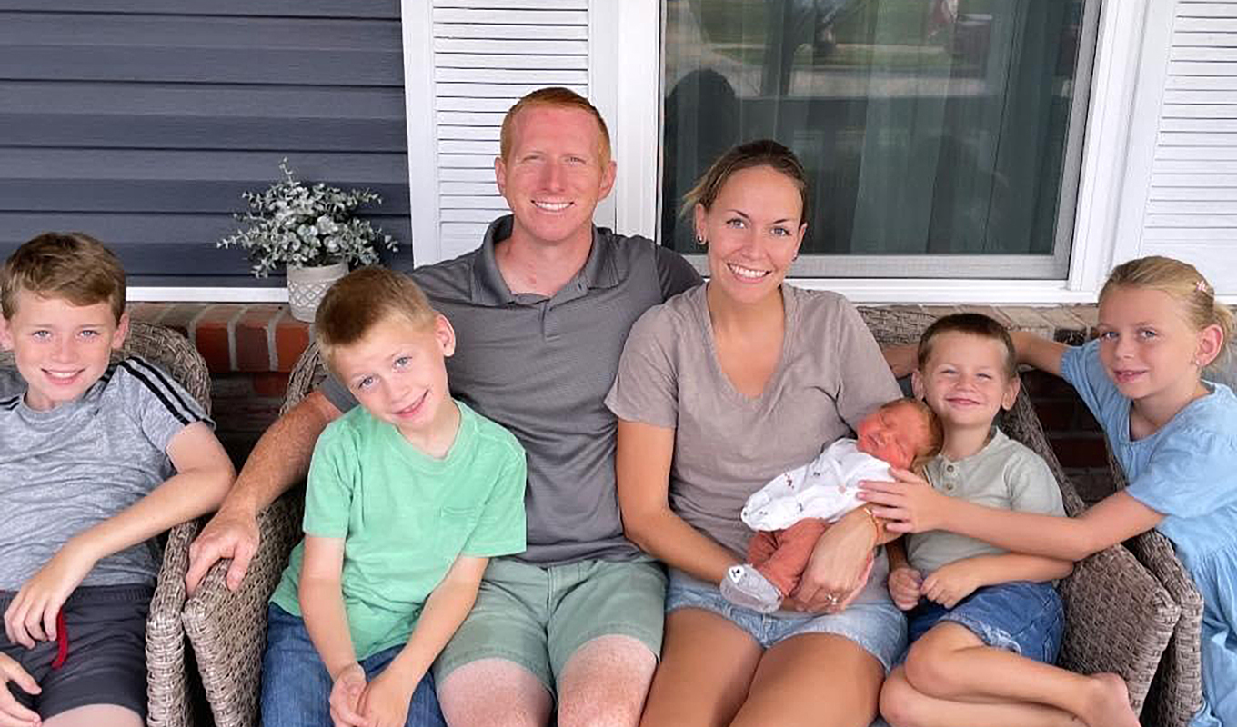 Large family sits on front porch with mom holding baby.