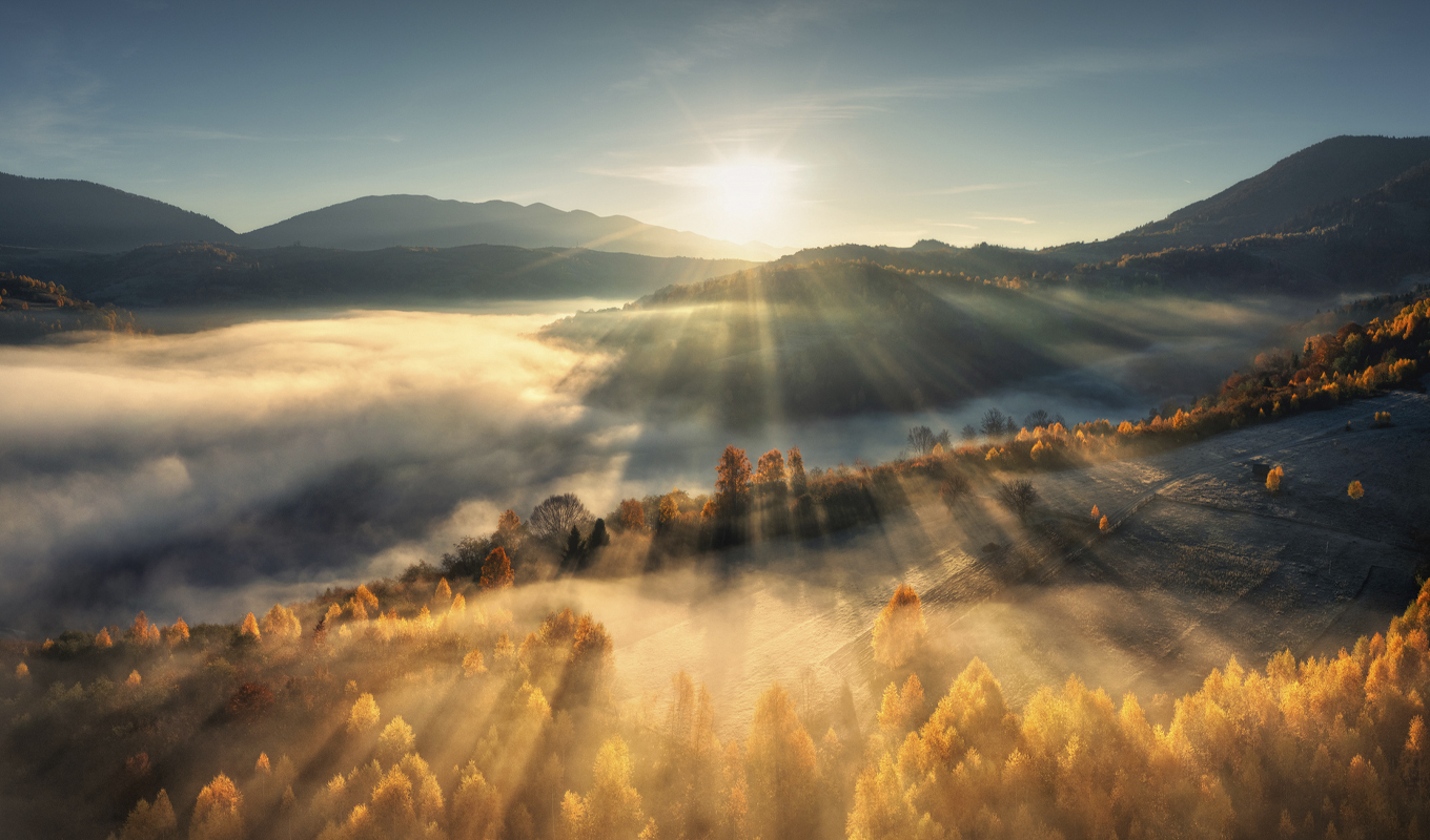 Sunlight pierces fog, illuminating the serene mountain landscape in a captivating display of nature's beauty.