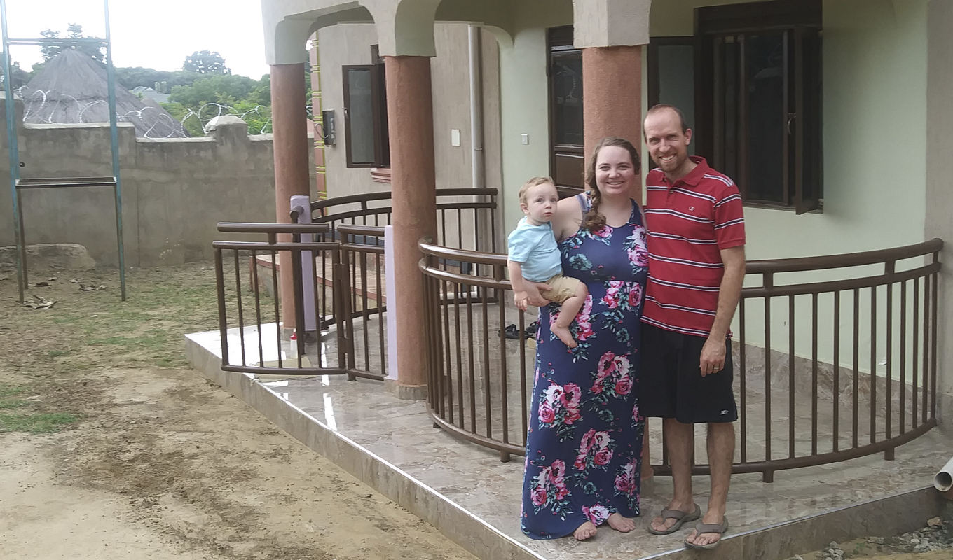 A man and woman hold a baby while standing in front of their house.
