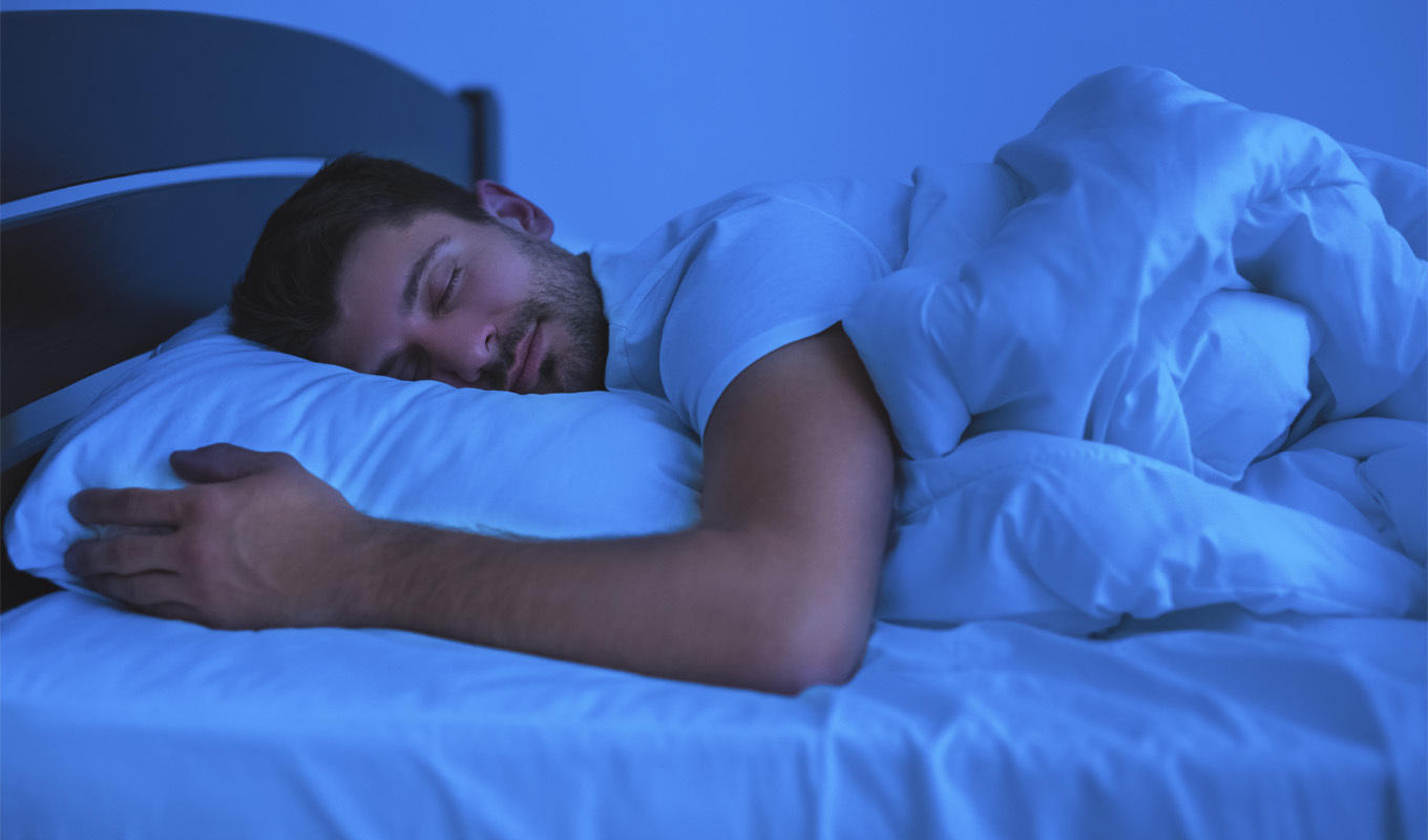 A man peacefully sleeping in bed, his eyes gently closed, surrounded by soft bedding and a serene atmosphere.