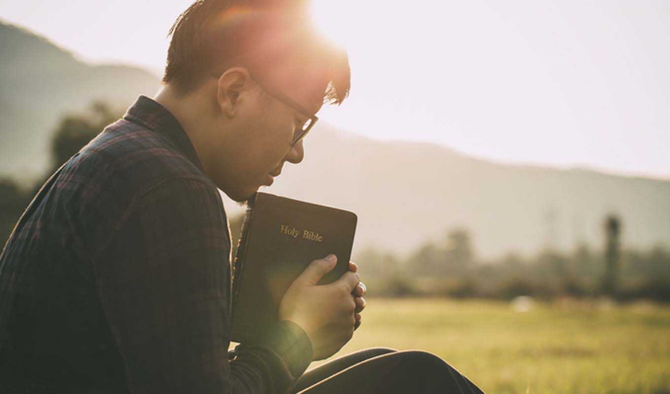 Man praying in the morning, outdoors with his Bible