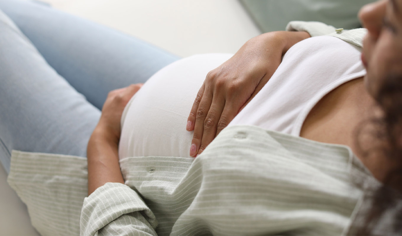 Pregnant woman resting on a couch with hands on growing belly.