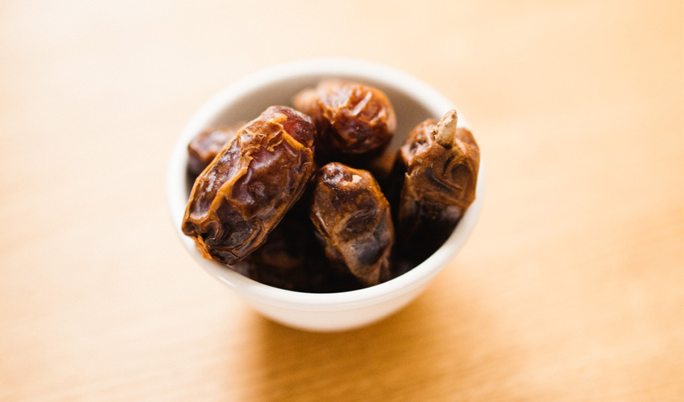 Bowl of dried dates on a light wooden surface.