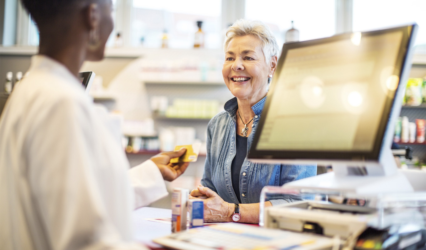 A smiling woman concludes a transaction at a pharmacy with a helpful clerk.