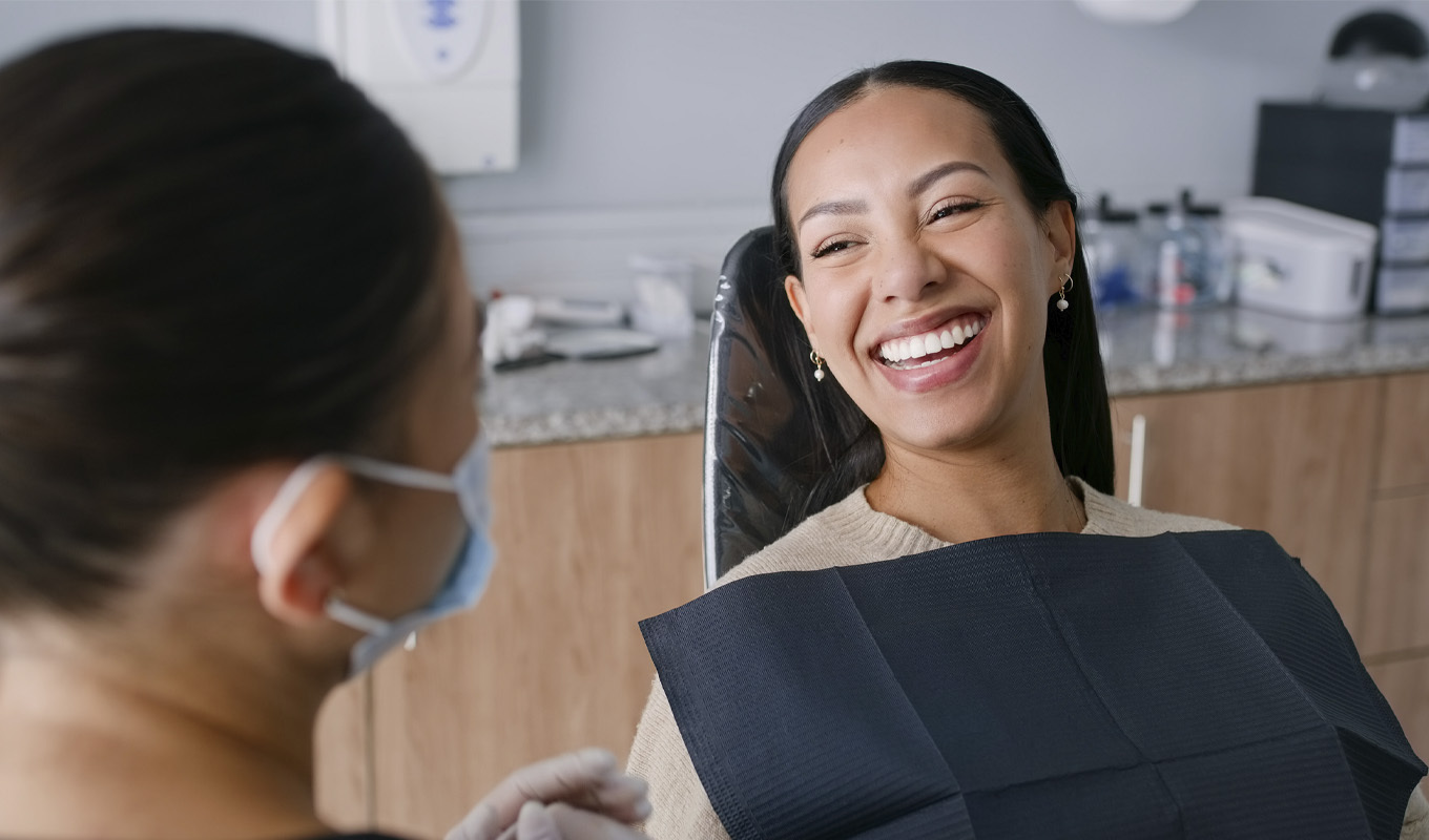 A woman smiles confidently while seated in a dental chair, showcasing a positive dental experience.