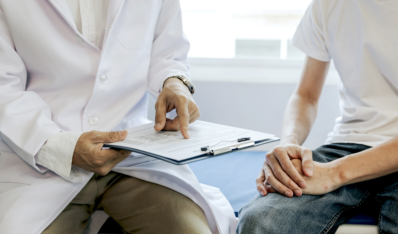 A doctor with a clipboard explains a procedure to a man in jeans and a T-shirt.