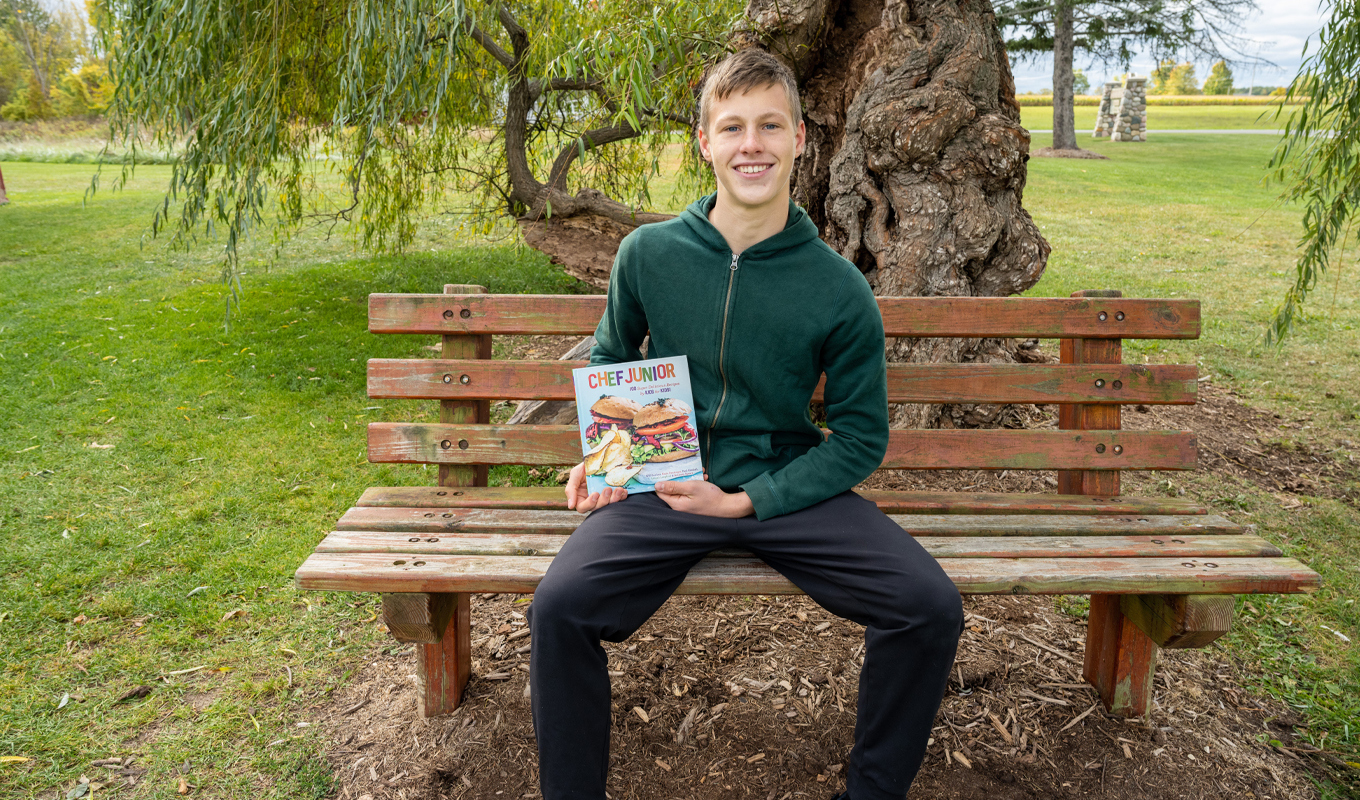 A young man sitting on a bench, holding a book, immersed in reading while enjoying the tranquility of his surroundings