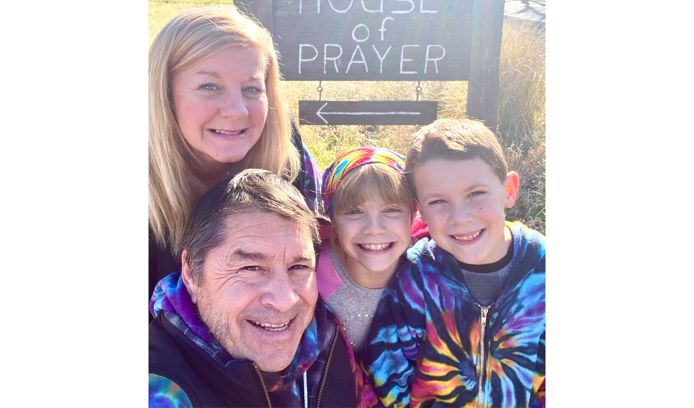 A family stands together smiling in front of a sign for a house of prayer, capturing a moment of unity and faith.