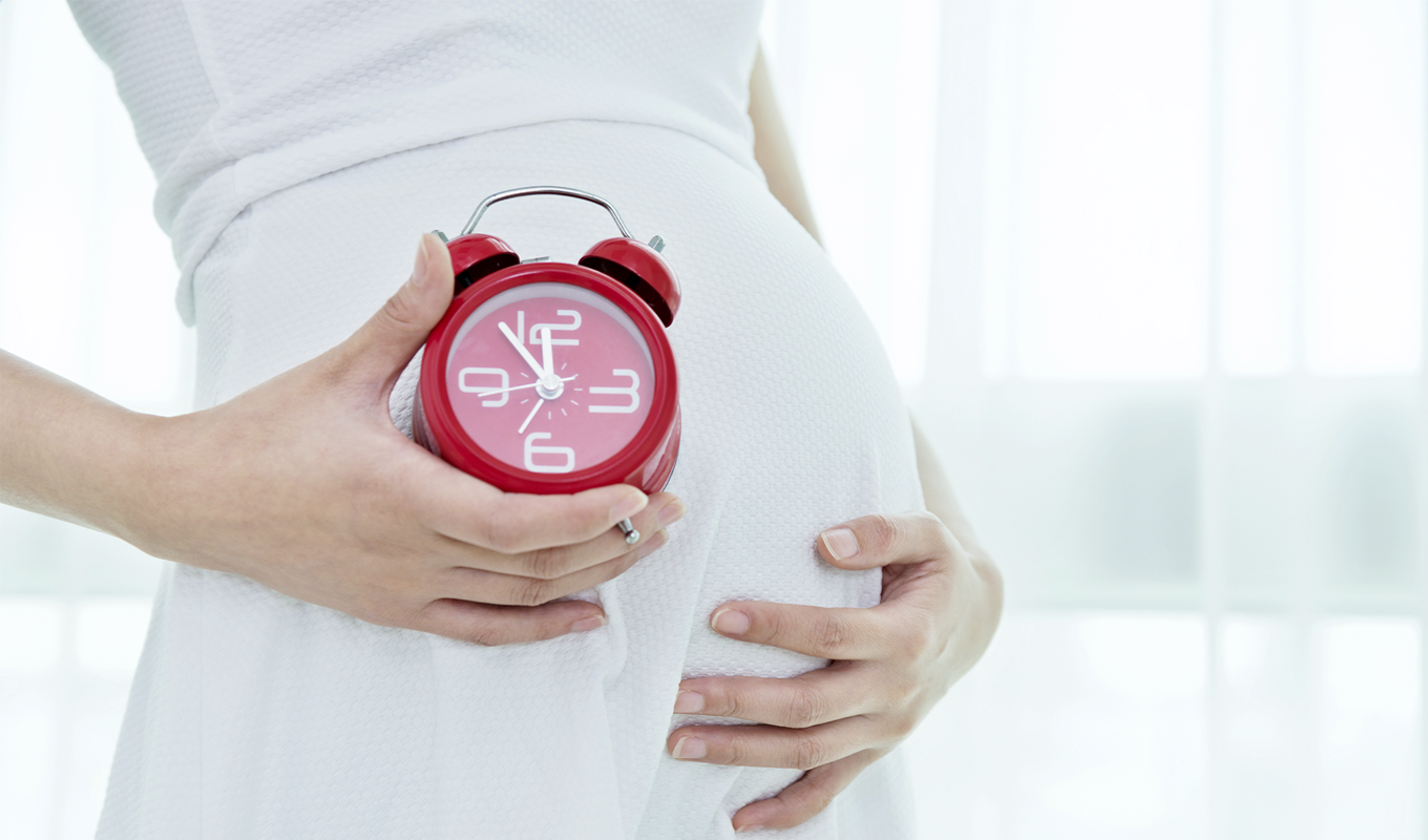 Pregnant woman holding an alarm clock up to her belly