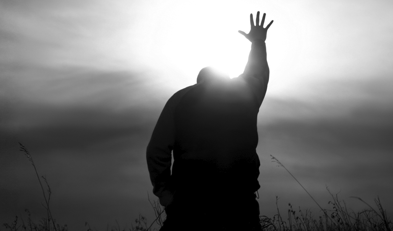 Silhouette of a man solemnly raising his hand to the sky