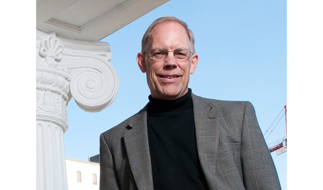 A man in glasses and a black turtleneck standing in front of a building.