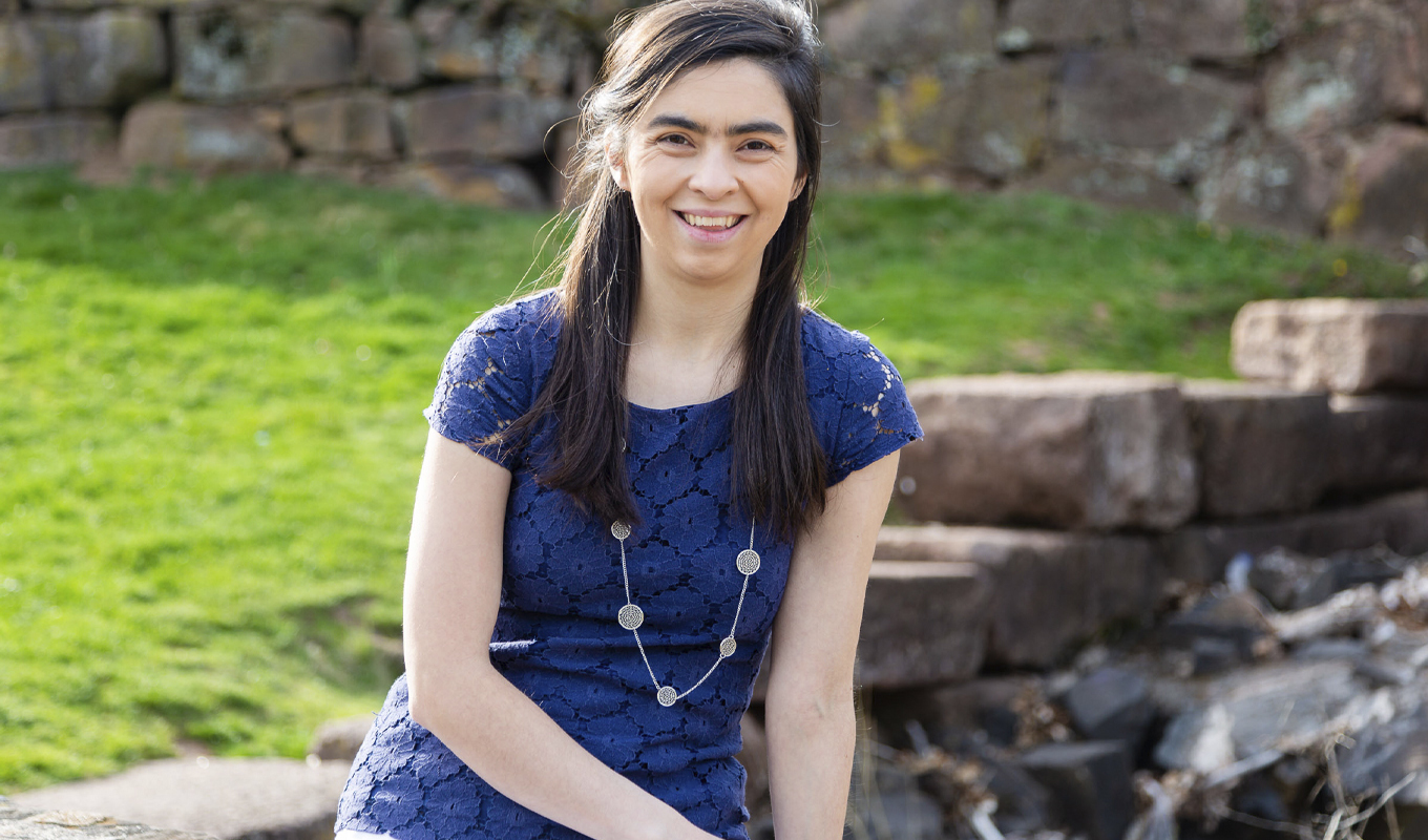 A young woman in a blue dress sits gracefully on a rock, surrounded by nature's beauty.