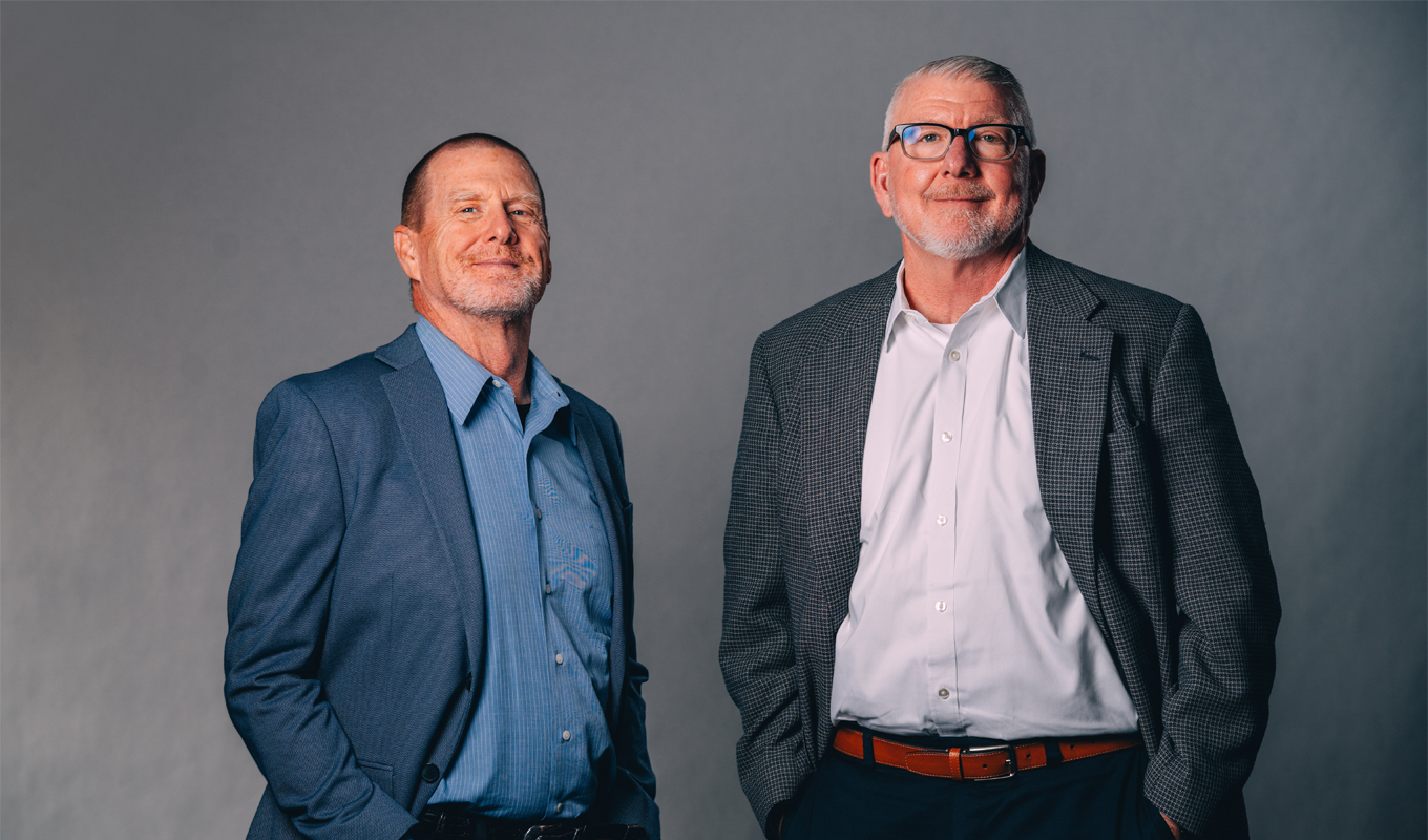 Two men dressed in business casual clothing look seriously at the camera.