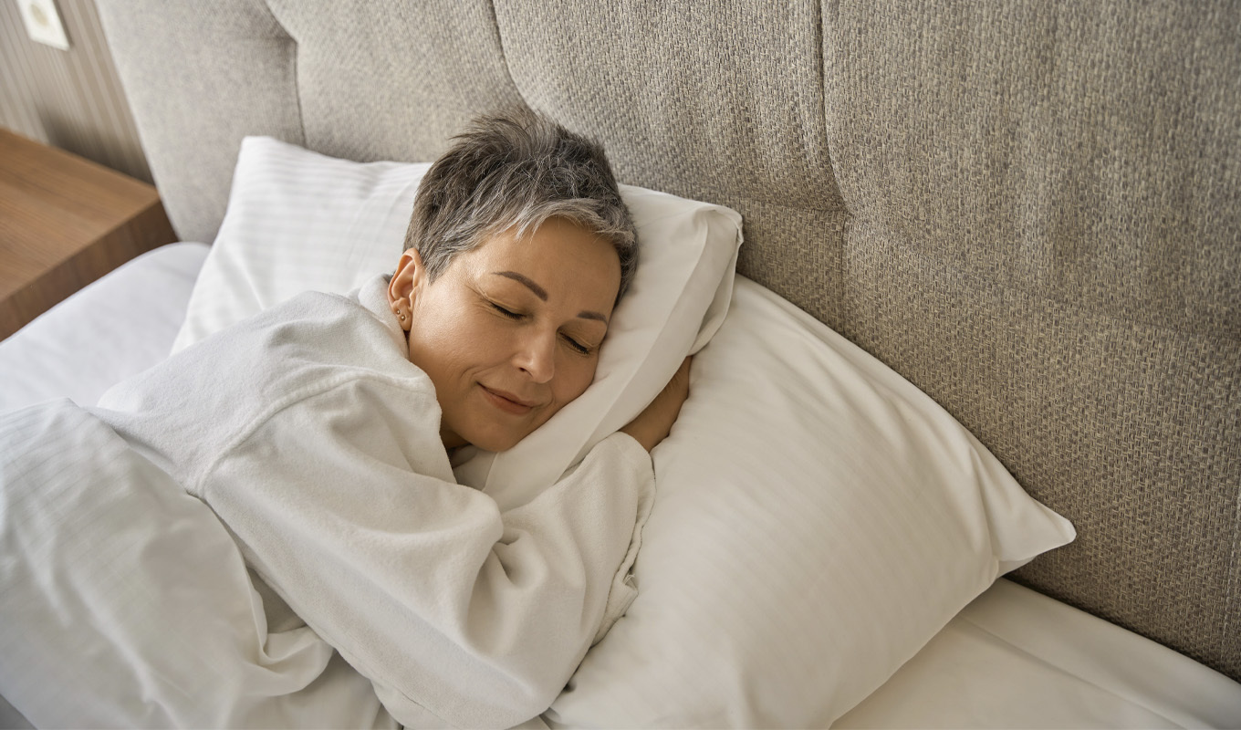 A woman peacefully sleeping in bed, her eyes gently closed, surrounded by soft bedding and a serene atmosphere.
