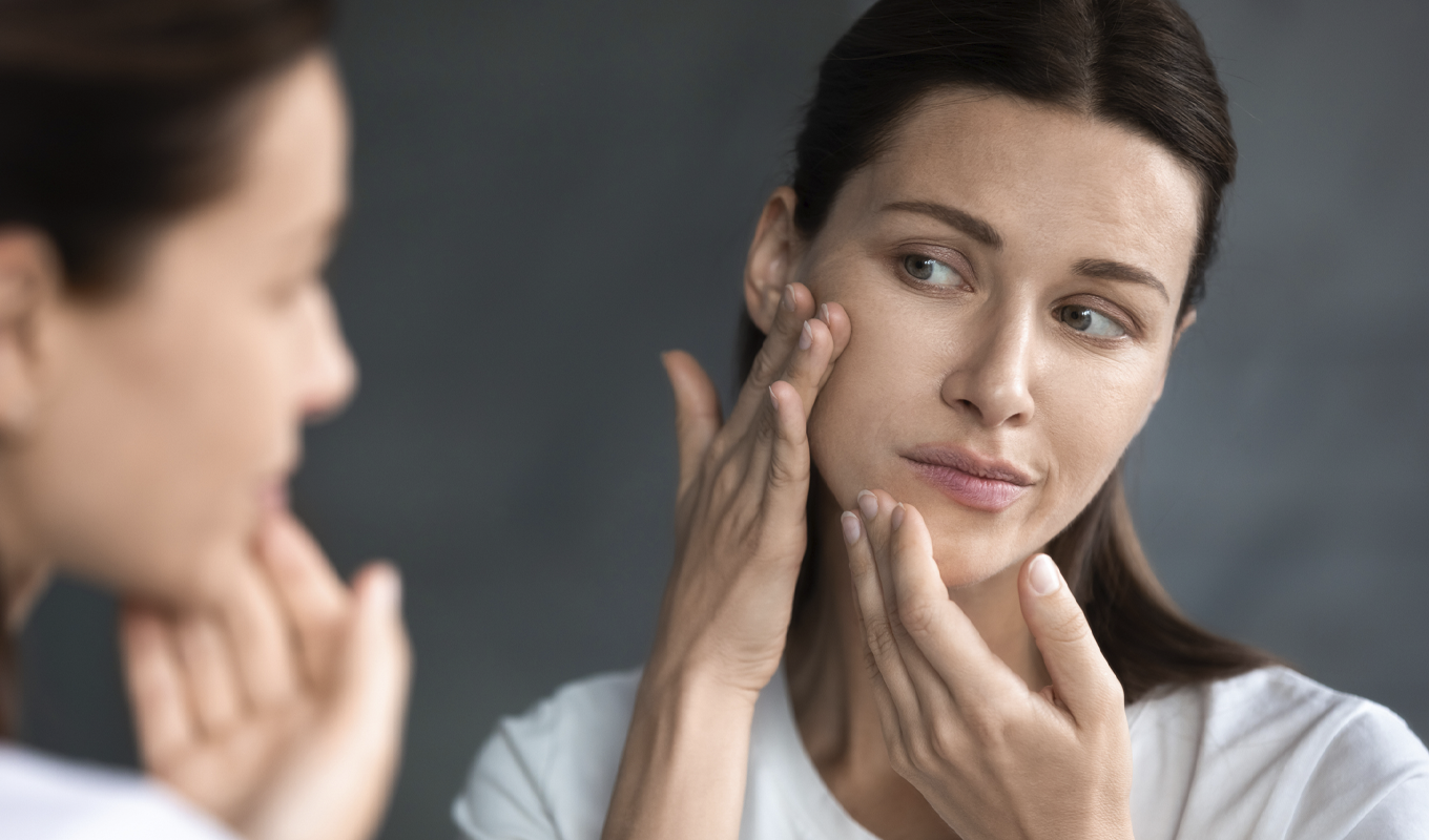 A woman checks the skin on her cheek in a mirror.