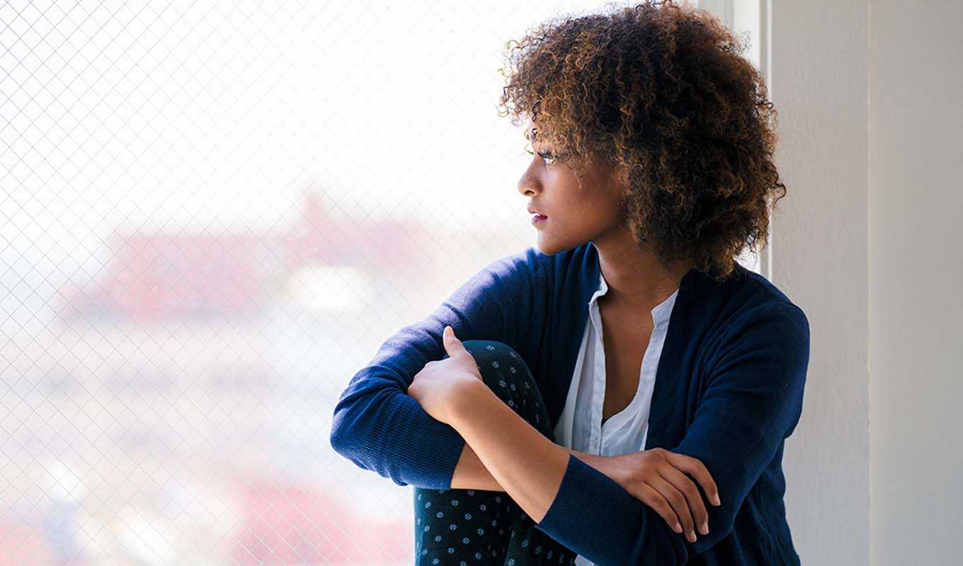 Solemn woman looking out a bay window