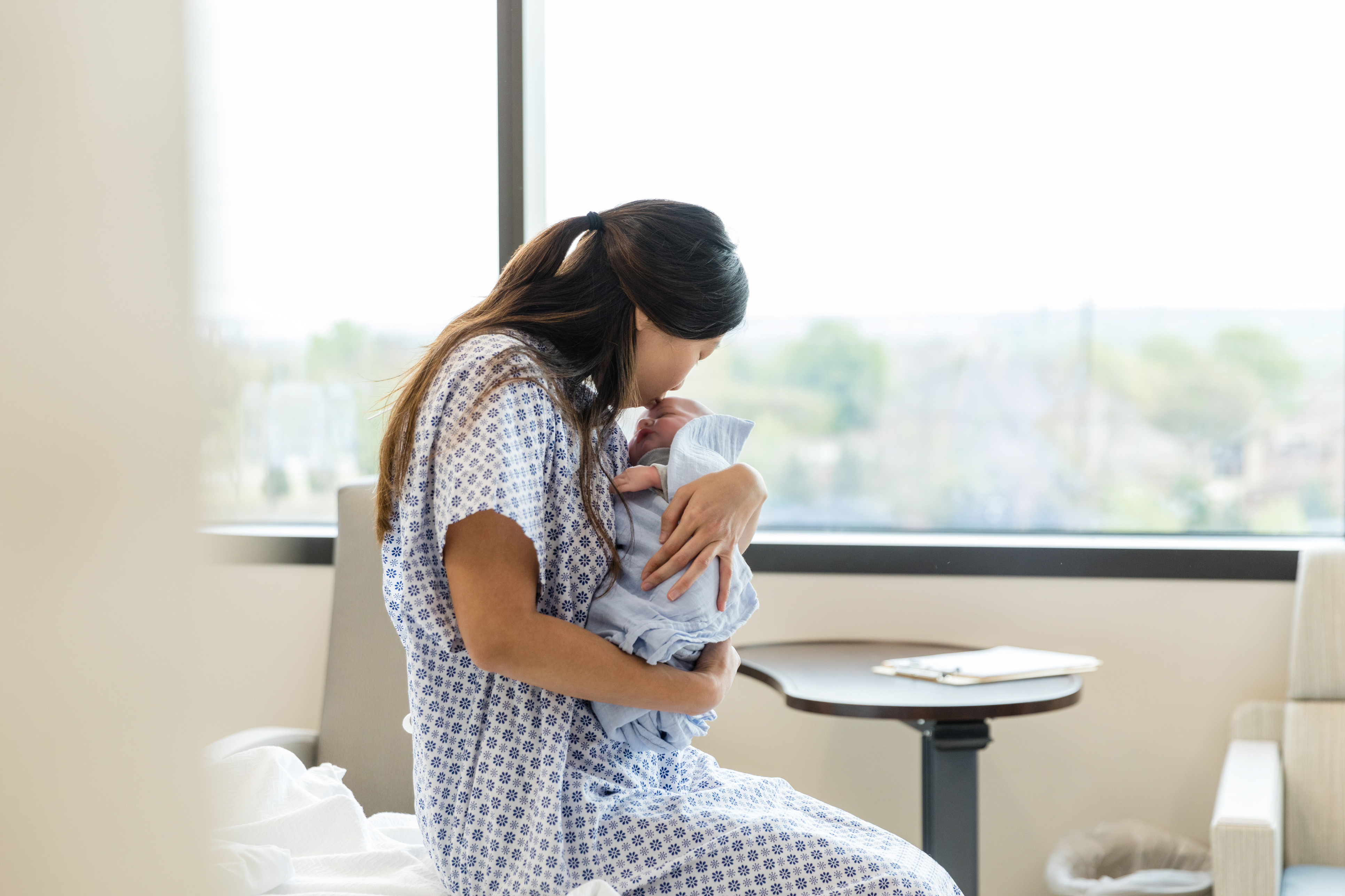 A woman in a hospital gown lovingly cradles her newborn baby, showcasing a tender moment of motherhood.